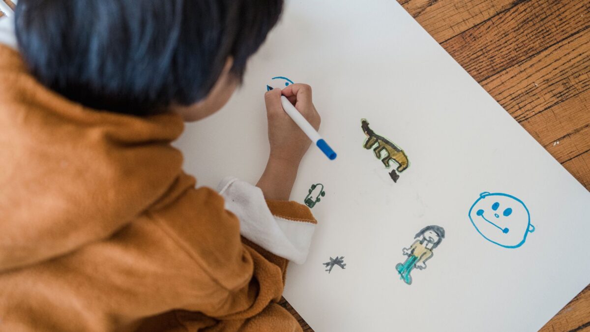 A child creating drawings with markers on paper while sitting indoors.
