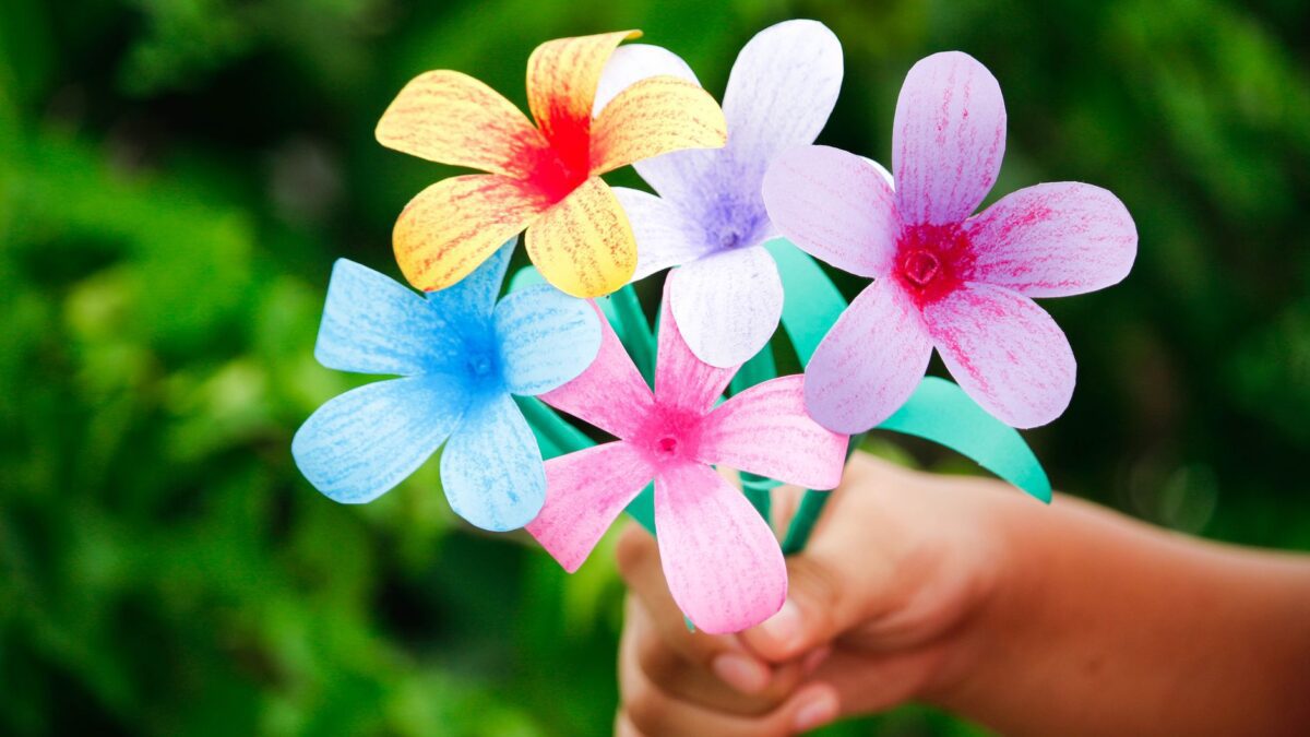 Colorful handmade paper flowers held in a hand against a lush green background, showcasing creativity and DIY art.