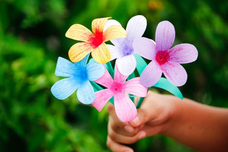 Colorful handmade paper flowers held in a hand against a lush green background, showcasing creativity and DIY art.